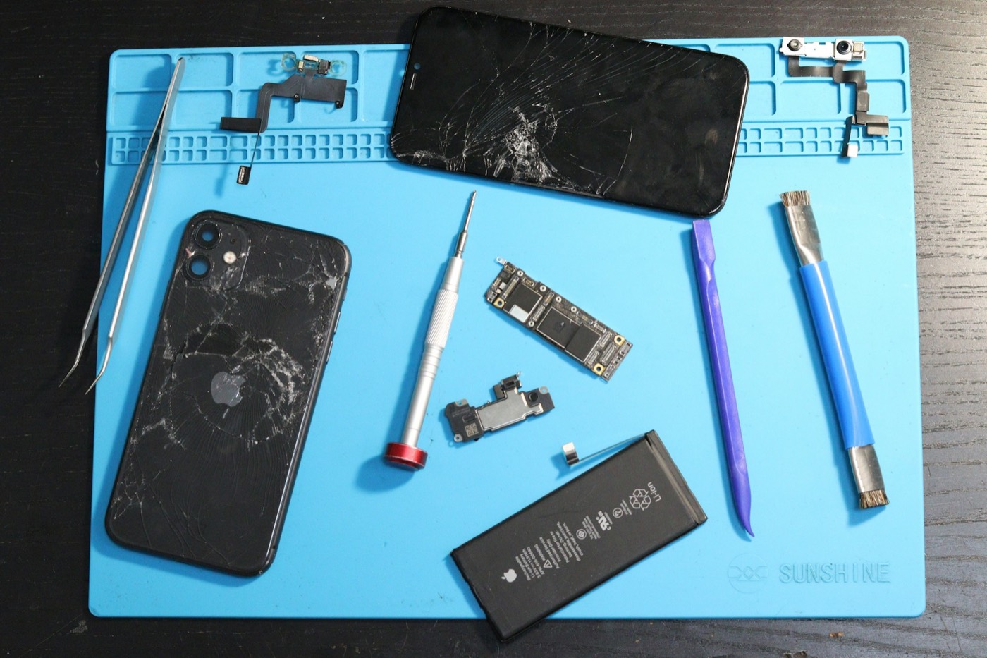 Celular desmontado sobre bancada de reparo, com ferramentas e pecas separadas